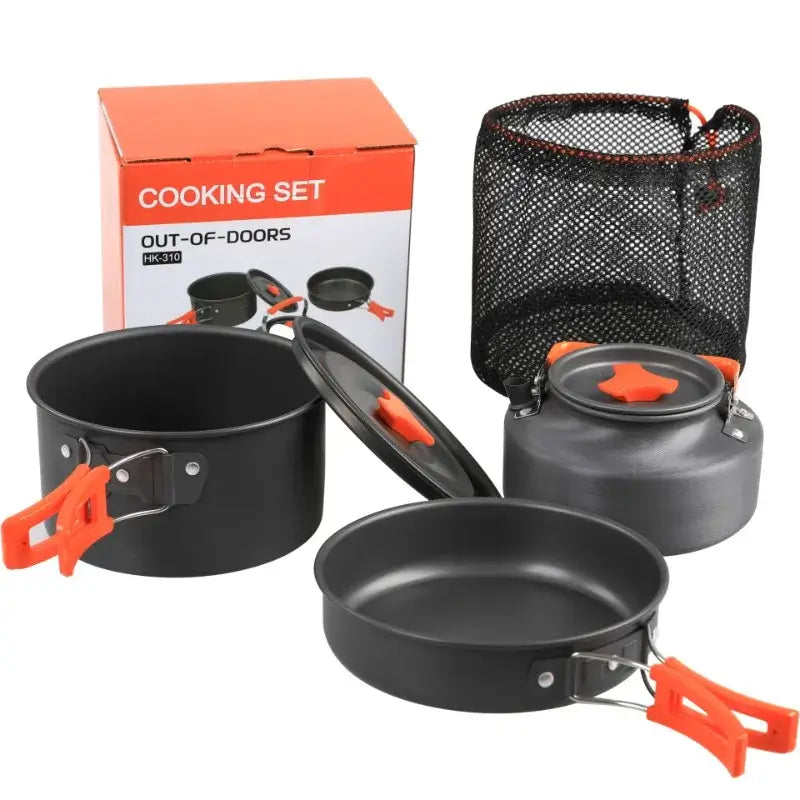 Portable camping cookware set including pot, pan, and kettle with orange handles in packaging for outdoor cooking.