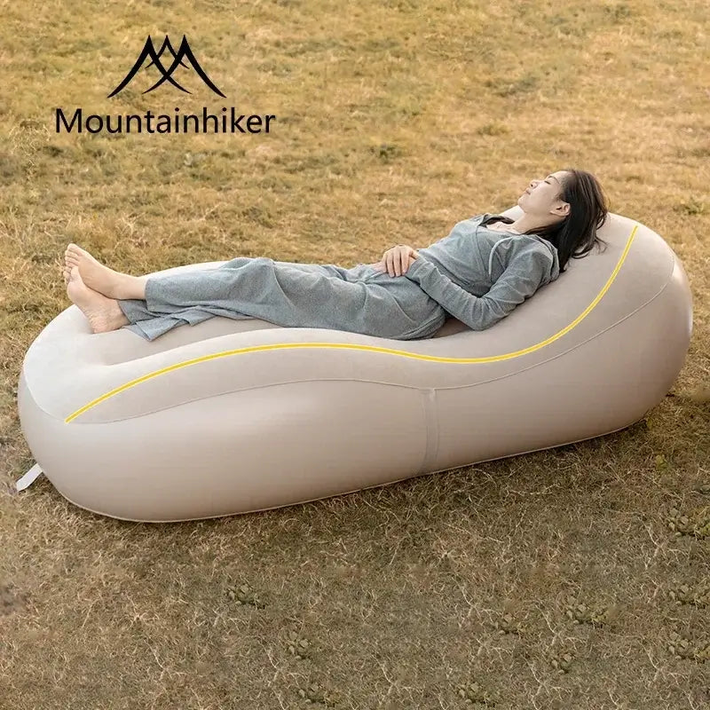 Woman relaxing on a Fast Inflatable Air Sofa Bed by Mountainhiker, enjoying outdoor comfort in a grassy area.