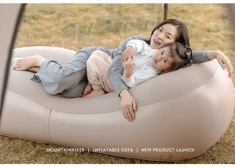 Mother and child relaxing on a beige inflatable sofa in a grassy outdoor setting.