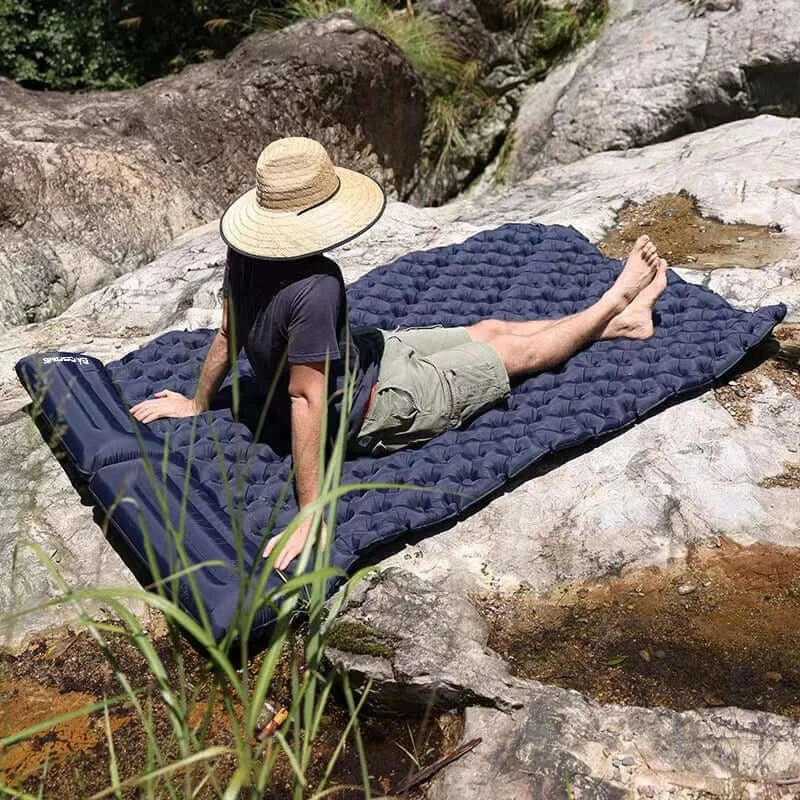 Person lounging on an outdoor double inflatable mattress on rocks, ideal for camping and travel comfort.