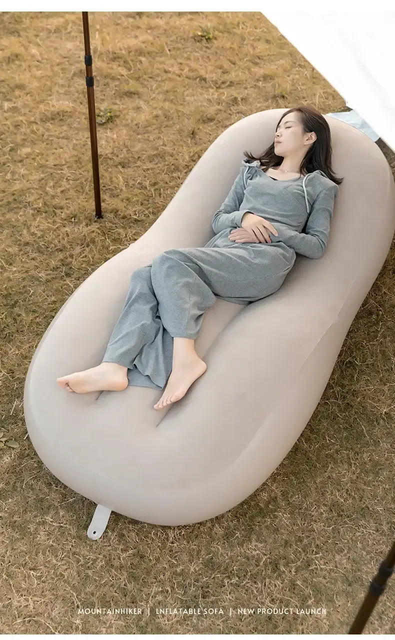 Woman relaxing on a fast inflatable air sofa bed outdoors on grass, showcasing comfort and convenience.