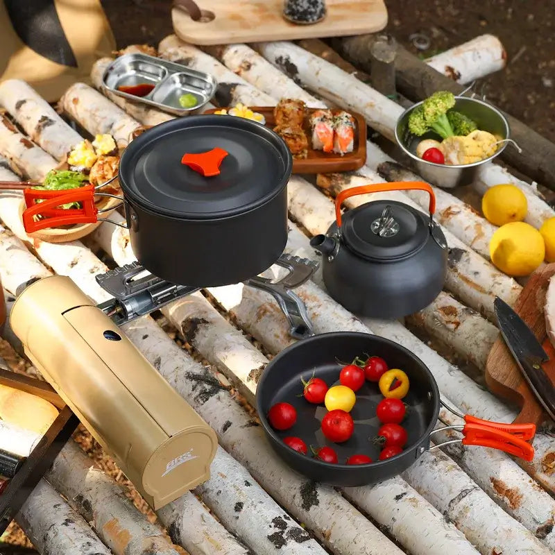 Portable camping cookware set on a wooden table, featuring pots, kettle, and fresh vegetables, ideal for outdoor cooking.